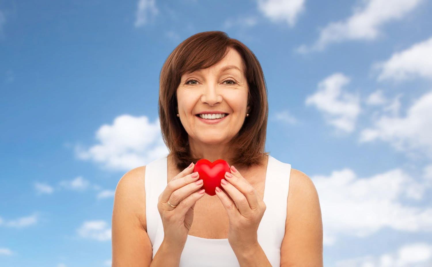 portrait of smiling senior woman holding red heart