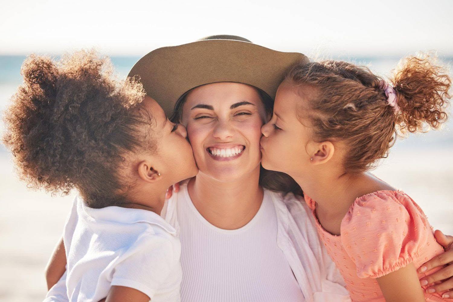 happy family and girl with mother at beach kissing and bonding